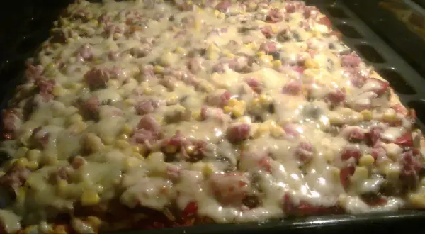 Pyszne ciasto do pizzy z serem, kukurydzą i wędliną, pieczone w piekarniku. Idealne na rodzinny obiad.