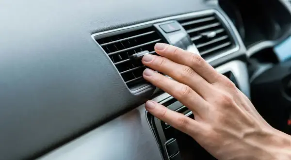 Dłoń reguluje nawiew klimatyzacji w samochodzie, by zapewnić komfortową podróż.