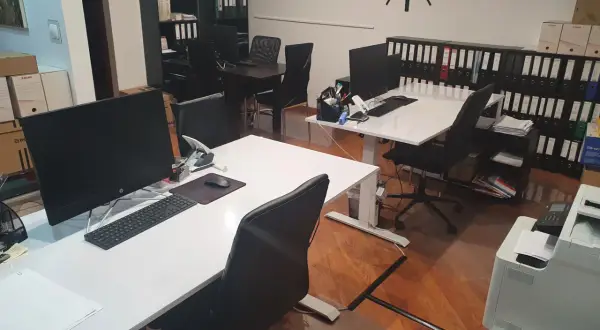 Nowoczesne biuro z biurkami, komputerami, regałami z segregatorami i zegarem na ścianie.