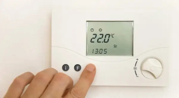 Dłoń naciska przycisk na termostacie pokazującym 22°C.