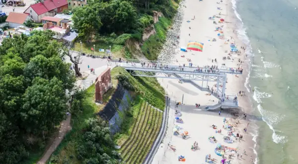 Widok na plażę z kładką i ruinami. Ludzie odpoczywają na piasku, ciesząc się atrakcjami nad morzem.