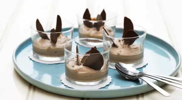 Fyra glas med len choklad dessert, dekorerade med chokladflarn, står på en turkos bricka. En perfekt avslutning på middagen.