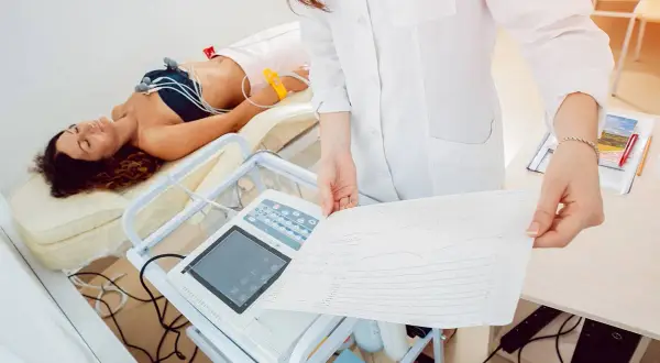 Une patiente allongée, connectée à un électrocardiogramme, pendant que le médecin examine le tracé. Voici comment se passe un électrocardiogramme.