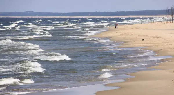 Plaża nad wzburzonym morzem, dwie osoby spacerują brzegiem.