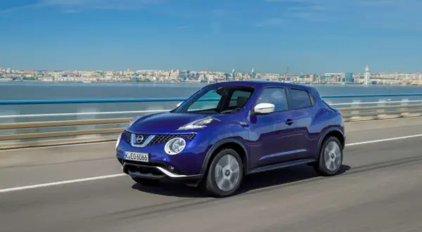 En blå Nissan Juke kör på en bro med en stad i bakgrunden. En perfekt bild för ett nissan juke test.