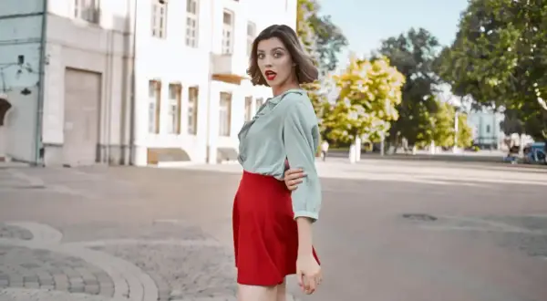 Kobieta w miętowej bluzce i czerwonej spódnicy, zastanawia się, jaka bluzka do czerwonej spódnicy pasuje najlepiej.