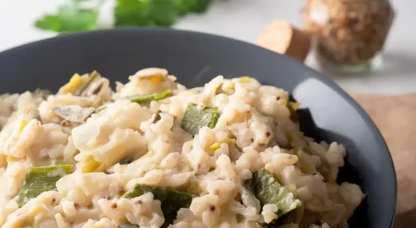 Un crémeux risotto poireaux, parsemé de grains de moutarde, servi dans un bol gris.