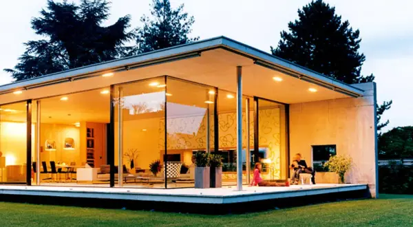 Ein moderner Bungalow mit Glasfronten und einem flachen Dach. Eine Familie entspannt sich auf der Terrasse.