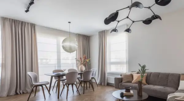 Nowoczesne oświetlenie salonu z jadalnią: designerska lampa nad stołem i reflektory na suficie tworzą przytulną atmosferę.