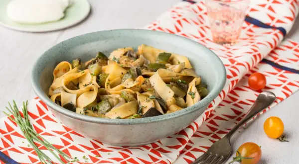 Un plat de pâtes one pot aux légumes d'été, courgettes, aubergines et champignons, garni d'herbes fraîches.