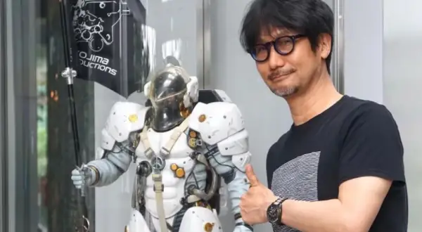 Hideo Kojima z kciukiem w górę obok postaci z gry, z logo Kojima Productions w tle.