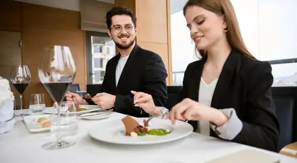 Elegancki strój na kolację do restauracji. Para w garniturach delektuje się wykwintnym deserem przy kieliszkach czerwonego wina.
