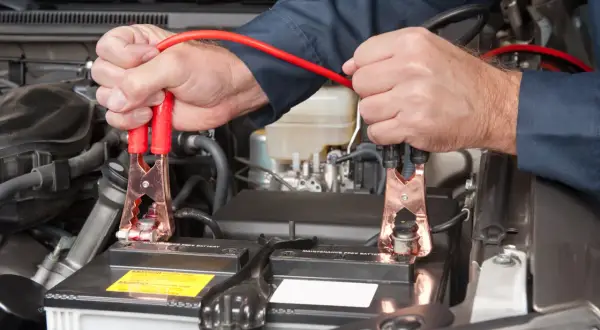Ręce mechanika podłączają kable rozruchowe do akumulatora samochodowego, rozpoczynając czas ładowania akumulatora.
