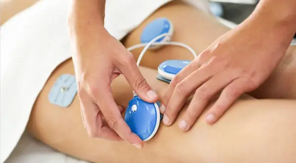 Dłonie terapeuty umieszczają elektrody do elektrostymulacji na udzie pacjenta.