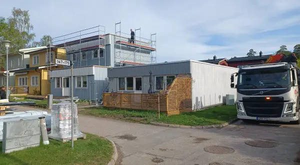 Byggnadsarbetare på ställningar vid hus som ska bygga till. En kranbil står parkerad.