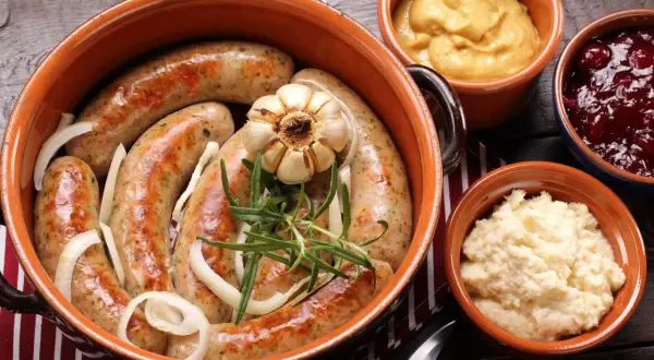 Pyszna kiełbasa z piekarnika w glinianym naczyniu, z cebulą, czosnkiem i rozmarynem. Obok musztarda, żurawina i chrzan.