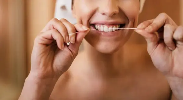 Donna sorridente che mostra come usare il filo interdentale per una pulizia profonda dei denti.