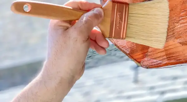 Mano aplicando barniz a madera de pino para exterior. Protegiendo la madera para que dure más.