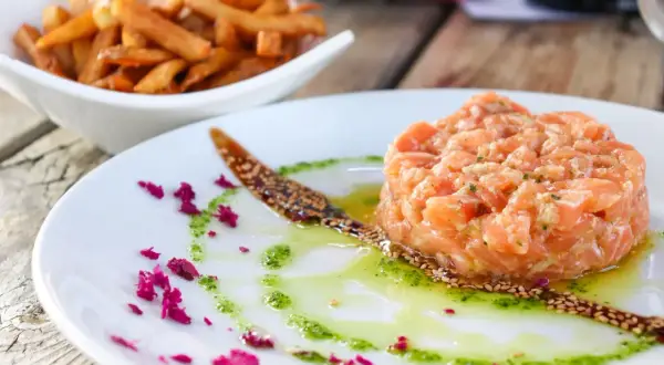 Tatar z łososia do sushi, podany z sosem i posypką z sezamu, obok miseczki frytek.