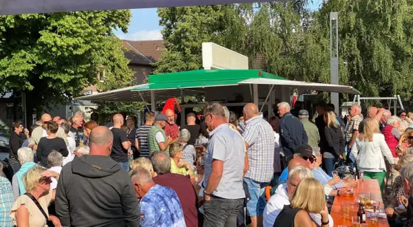 Menschen genießen den feierabendmarkt heute. Viele stehen an einem Imbisswagen, andere sitzen an orangefarbenen Tischen.