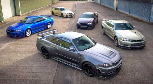 Pięć kultowych Nissanów GT-R R34 w różnych kolorach, stojących na betonowym placu.