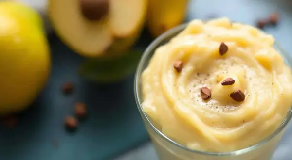 Un bol de compote de pêche onctueuse, garnie d'amandes et de cannelle, avec des pêches fraîches en arrière-plan.