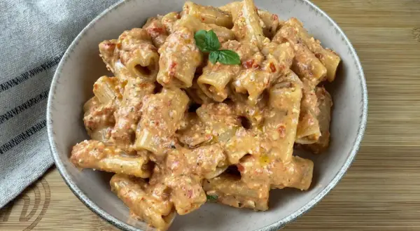 Rigatoni conditi con un cremoso pesto di pomodorini e ricotta, guarniti con basilico fresco.