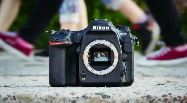 Nikon D500 na kamieniu, w tle nogi ludzi. Chcesz wiedzieć, jak sprawdzić przebieg aparatu?