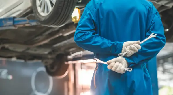 Meccanico in tuta blu con chiavi inglesi, pronto per i tagliandi auto. L'auto è sollevata sul ponte.