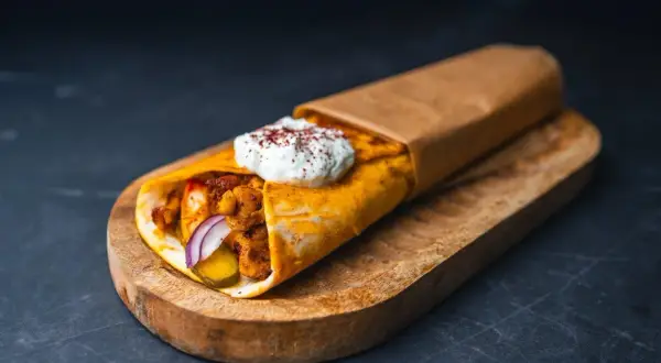 Pyszna shoarma drobiowa z sosem jogurtowym i przyprawami, zawinięta w placek, podana na drewnianej desce.