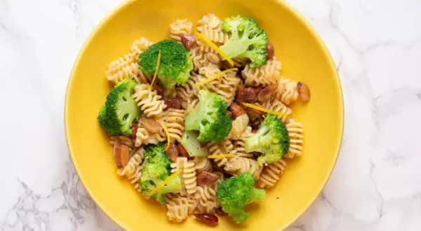 Macarrones con brócoli, trozos de salchicha y ralladura de limón en un plato amarillo.