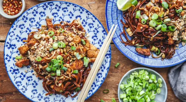 Två tallrikar med läcker pad thai, toppad med jordnötter och salladslök. Ett perfekt pad thai recept för en smakrik måltid.