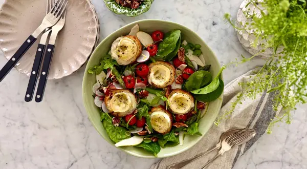 En härlig somrig mat-upplevelse med en fräsch sallad toppad med gratinerad getost på rostat bröd, körsbärstomater, rädisor och nötter.