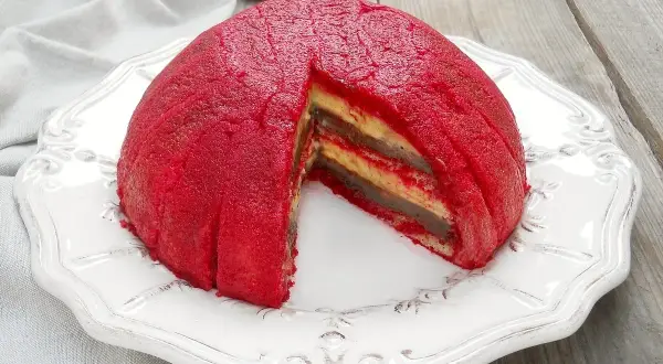 Zuppa inglese, un dessert a cupola con strati di crema e pan di Spagna, ricoperto da una glassa rossa vibrante.