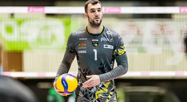 Bartłomiej Lipiński, siatkarz w szarym stroju z numerem 1, trzyma piłkę do siatkówki.