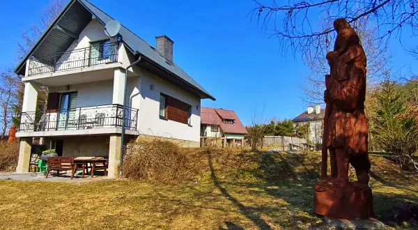 Dom z balkonami i drewniana rzeźba w ogrodzie.