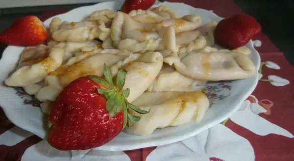 Pyszne pierogi z truskawkami, polane roztopionym masłem, ozdobione świeżymi owocami.