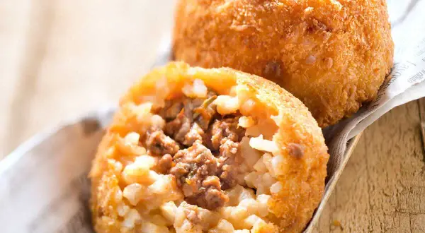 Deux arancini bolognaise dorés et croustillants, l'un ouvert révélant un cœur de riz et de viande savoureux.