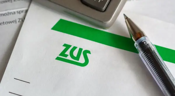 Długopis i kalkulator leżą na papierze z logo ZUS. Czas na rozliczenie składek społecznych.