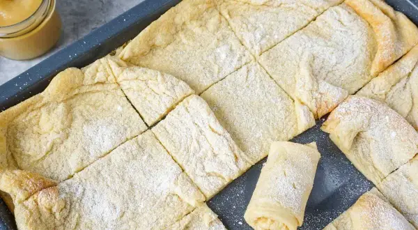 Frisch gebackener Ofenpfannkuchen, in Quadrate geschnitten und mit Puderzucker bestäubt. Ein einzelnes Stück ist aufgerollt und zeigt die Füllung.