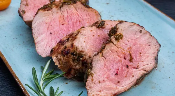 Saftiges Schweinefilet, perfekt gegrillt. Die Kerntemperatur ist entscheidend für dieses zarte Ergebnis. Rosmarin und Tomaten garnieren den Teller.