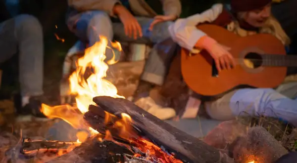 Przy ognisku rozbrzmiewają znane piosenki. Ktoś gra na gitarze, a wokół gromadzą się przyjaciele, ciesząc się wspólnym wieczorem.