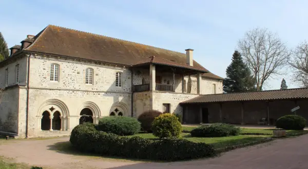 Bâtiment en pierre avec des arches romanes, un balcon et un jardin.