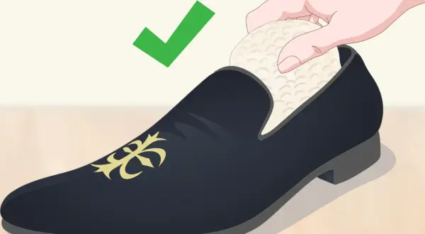 Une main insère un embauchoir dans une chaussure de ville noire ornée d'un motif doré. La mise en forme des chaussures est essentielle pour leur longévité. ✅