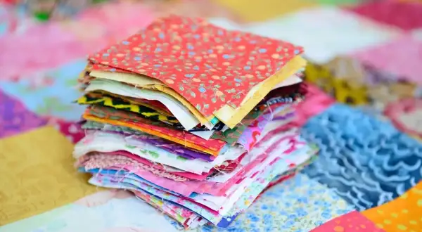Stos kolorowych kwadratów materiałów, gotowych do stworzenia patchworku. To właśnie patchwork – sztuka łączenia skrawków tkanin w piękne wzory.