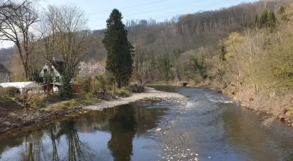 Idyllische Flusslandschaft am Wupperhof Solingen mit Fachwerkhäusern und bewaldeten Hängen.