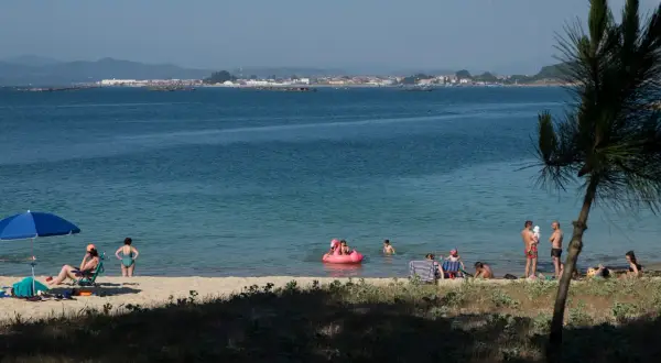 Gente disfruta de un día soleado en las playas de O Grove, con niños jugando en el agua y adultos relajándose en la arena.