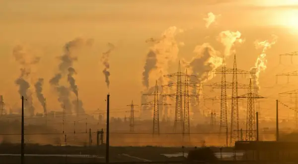 Dymiące kominy fabryk i linie energetyczne na tle zachodzącego słońca symbolizują antropogeniczne zmiany klimatu.