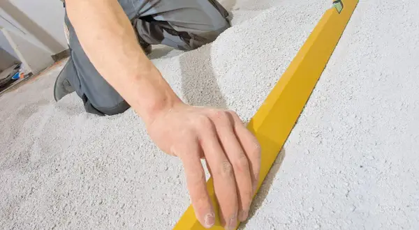 Hand gleicht Schüttung für trockenestrich verlegen mit Richtlatte aus.