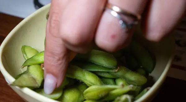Ręka sięga po zielone strączki edamame w miseczce. Zdrowa przekąska, co zamiast Controloc?